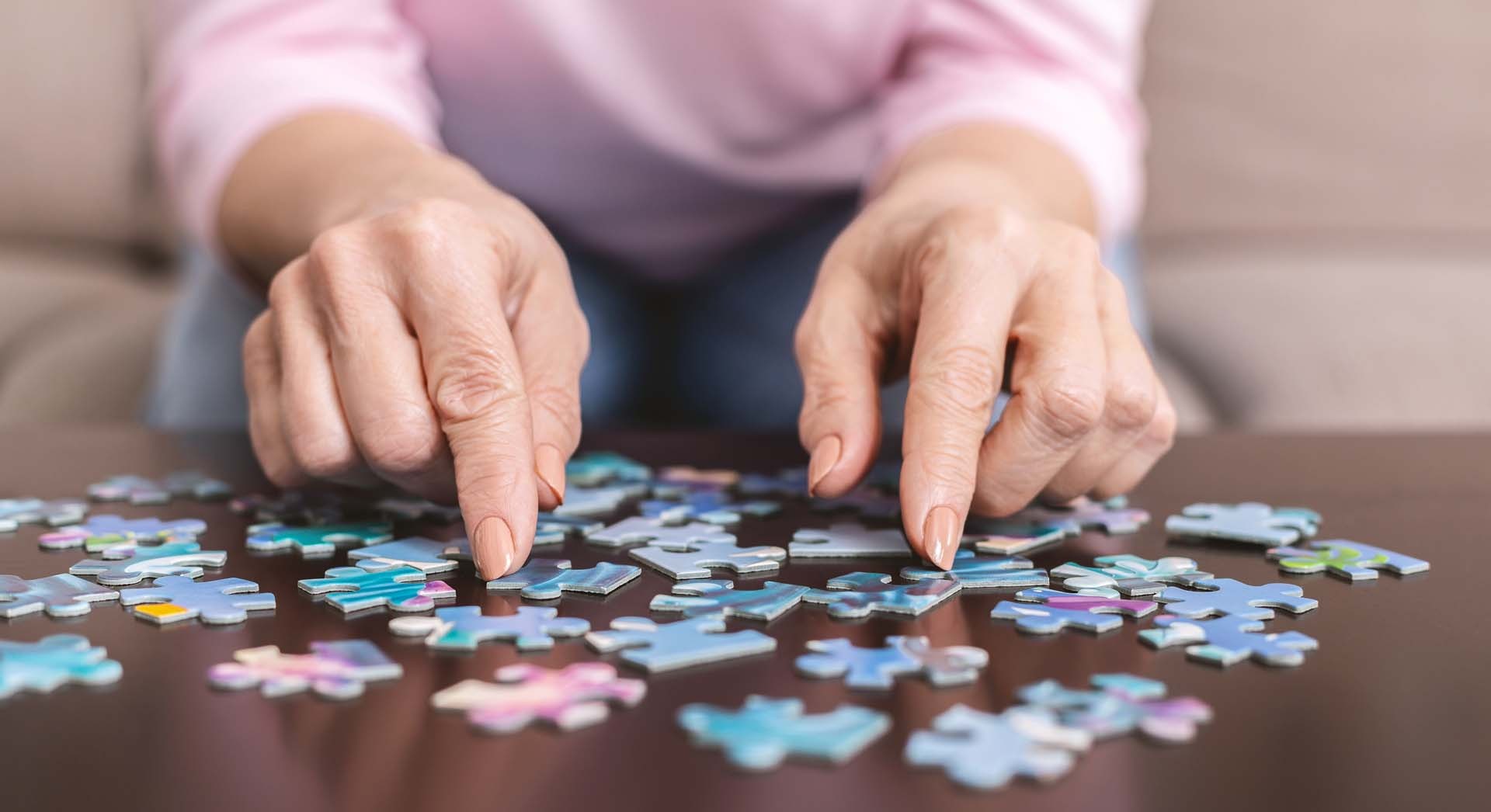 Elderly woman hands doing jigsaw puzzle closeup - Calm Seas Home Care Close-up of an elderly person assembling a jigsaw puzzle on a dark tabletop.