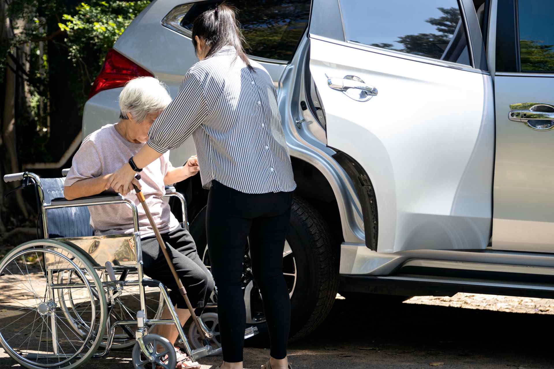 Calm Seas Home Care - Calm Seas Home Care Caregiver helping an elderly woman in a wheelchair prepare to enter a silver SUV with its door open.